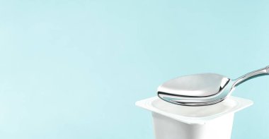 Yoğurt kabı ve nane arkaplanda gümüş kaşık yoğurt kremalı beyaz plastik kap sağlıklı beslenme ve beslenme dengesi için taze süt ürünü.