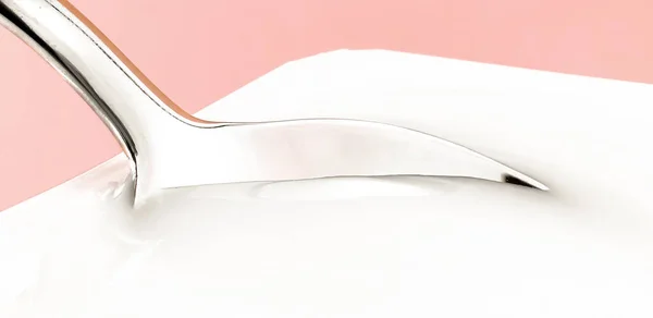 Tazza di yogurt e cucchiaio d'argento su sfondo beige, contenitore di plastica bianca con crema di yogurt, latticini freschi per una dieta sana e un equilibrio nutrizionale — Foto Stock