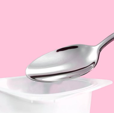 Yoğurt kabı ve pembe arka planda gümüş kaşık yoğurt kremalı beyaz plastik kap sağlıklı beslenme ve beslenme dengesi için taze süt ürünü.