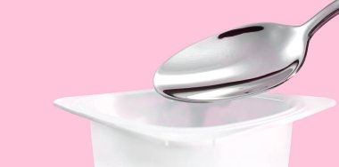 Yoğurt kabı ve pembe arka planda gümüş kaşık yoğurt kremalı beyaz plastik kap sağlıklı beslenme ve beslenme dengesi için taze süt ürünü.