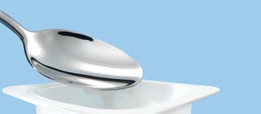 Yoğurt kabı ve mavi arka planda gümüş kaşık, beyaz plastik kap, sağlıklı beslenme ve beslenme için taze süt ürünü