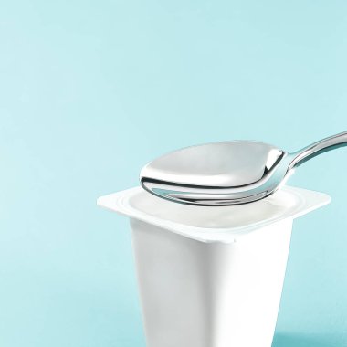 Yoğurt kabı ve nane arkaplanda gümüş kaşık yoğurt kremalı beyaz plastik kap sağlıklı beslenme ve beslenme dengesi için taze süt ürünü.