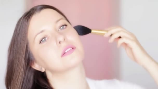 Mujer con cepillo cosmético aplicando maquillaje y sonrisa, retrato facial de belleza de modelo femenino caucásico sobre fondo rosa, idea de maquillaje natural, cosméticos y productos para el cuidado de la piel comercial — Vídeo de stock