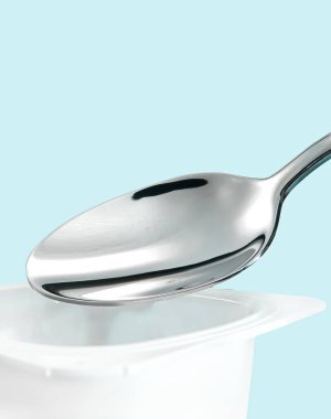 Yoğurt kabı ve nane arkaplanda gümüş kaşık yoğurt kremalı beyaz plastik kap sağlıklı beslenme ve beslenme dengesi için taze süt ürünü.