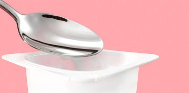 Yoğurt kabı ve pembe arka planda gümüş kaşık yoğurt kremalı beyaz plastik kap sağlıklı beslenme ve beslenme dengesi için taze süt ürünü.