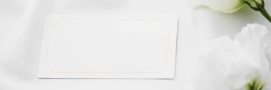 Düğün davetiyesi ya da hediye kartı ve beyaz gül çiçekleri düğün arkaplanı olarak düz kumaş üzerinde, boş kağıt ve tatil damgası, düz dizayn