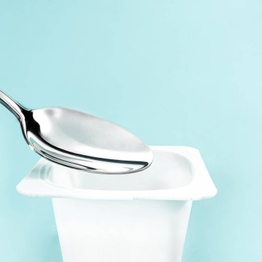 Yoğurt kabı ve nane arkaplanda gümüş kaşık yoğurt kremalı beyaz plastik kap sağlıklı beslenme ve beslenme dengesi için taze süt ürünü.