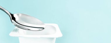 Yoğurt kabı ve nane arkaplanda gümüş kaşık yoğurt kremalı beyaz plastik kap sağlıklı beslenme ve beslenme dengesi için taze süt ürünü.