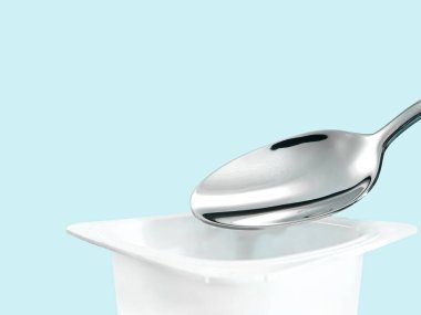 Yoğurt kabı ve nane arkaplanda gümüş kaşık yoğurt kremalı beyaz plastik kap sağlıklı beslenme ve beslenme dengesi için taze süt ürünü.