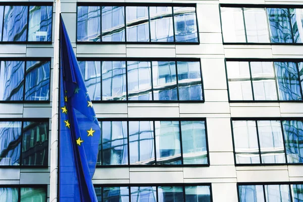 Bandera de la Unión Europea ondeando frente a un moderno edificio de oficinas corporativas, símbolo del Parlamento Europeo, la Comisión y el Consejo — Foto de Stock
