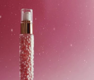 Pembe arka planda altın şişede cilt bakımı, kar ve Noel parıltısı