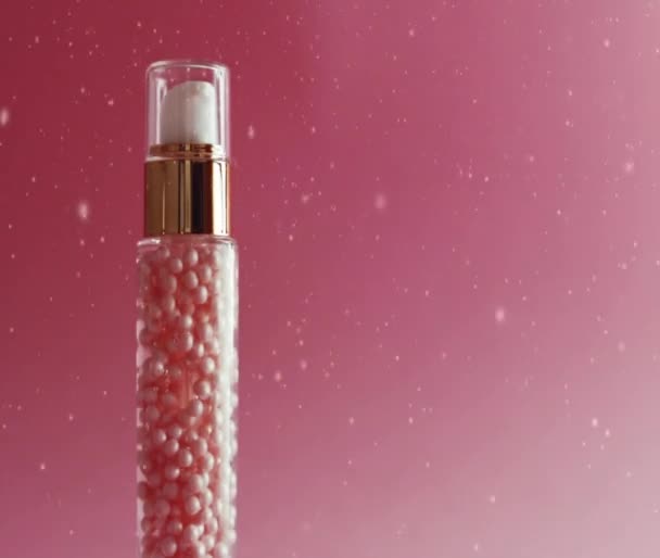 Produto Skincare em garrafa de ouro sobre fundo rosa, neve e brilho de Natal — Vídeo de Stock