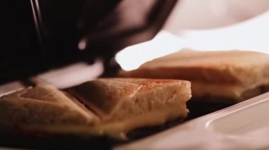 Sandviç tost makinesinde pişirilmiş sıcak üçgen peynirli sandviçler, ev yapımı konforlu yemekler.