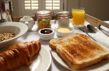 Breakfast tray offering croissant, toast, jam, butter, fruit salad, cereal, and orange juice. Cotswolds countryside, England