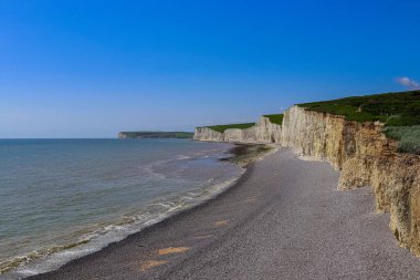 Seven Sisters towering white chalk cliffs at low tide, revealing a pebble beach along the scenic East Sussex coastline. East Sussex, England