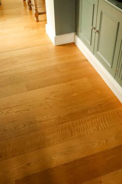Light oak hardwood flooring extending across a modern kitchen or living space, featuring sage green cabinetry and white baseboards