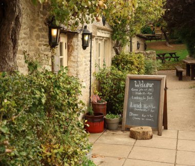 Eski bir İngiliz barına ev sahipliği yapan antika bir taş bina. İçinde ışıklı fenerler, hoş geldin tahtası ve bahçe masaları var. Cotswolds, İngiltere