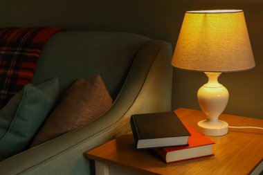 Rahat bir iç mekan, rahatlamak için sıcak bir atmosfer yaratıyor. Işıklı bir lamba, rahat bir koltuk ve kitaplar var.