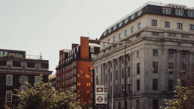 Tarihi binaların ve bir yeraltı istasyon tabelasının yer aldığı Londra şehir manzarası, İngiliz mimarisi ve toplu taşıma araçlarını belgeliyor