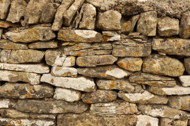 Kuru taş duvar, eski dokulu yüzeyi doğal kaya materyalleri ve taşların üzerinde yetişen engebeli yosunlarla sunuyor. Cotswolds, İngiltere