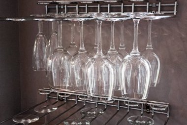 Krom bir rafta baş aşağı asılı duran temiz şarap kadehleri, bir barda, mutfakta ya da restoranda kullanılmaya hazır.