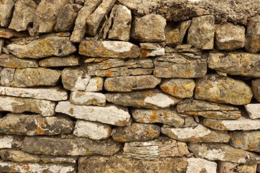 Kuru taş duvar, eski dokulu yüzeyi doğal kaya materyalleri ve taşların üzerinde yetişen engebeli yosunlarla sunuyor. Cotswolds, İngiltere