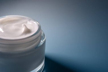 Beyaz kozmetik kremli cam kavanoz, cilt bakımı için nemlendirici, yüz ve vücut için güzellik ürünü, mavi bir stüdyo arka planında