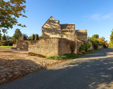 Antik taş ev ve doğal taş duvar, sıcak sonbahar güneşinin tadını çıkaran tarihi bir İngiliz köyünün bir kısmını oluşturuyor.