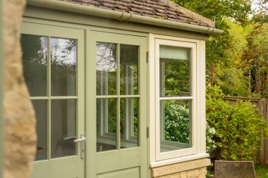 Evin dışı yeşil kapılı ve pencereli, yemyeşil bahçeli bitkileri ve doğal çevreyi yansıtıyor. Cotswold kırsal, İngiltere