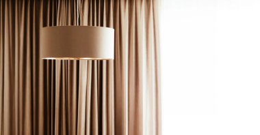 Sıcak bir kolye ışığı ve akıcı bej kahverengi perdelerle donatılmış minimalist iç mekan, metin için yumuşak bir arkaplan sağlar