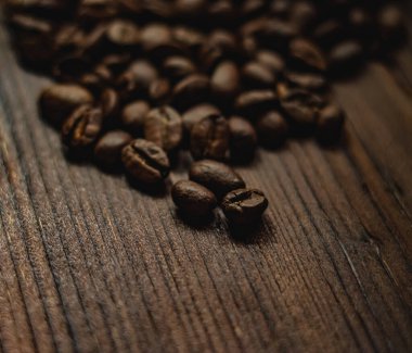 Kavrulmuş kahve çekirdekleri antik ahşap bir yüzey üzerinde zengin bir doku oluşturarak canlandırıcı bir espresso kokusu uyandırıyor.