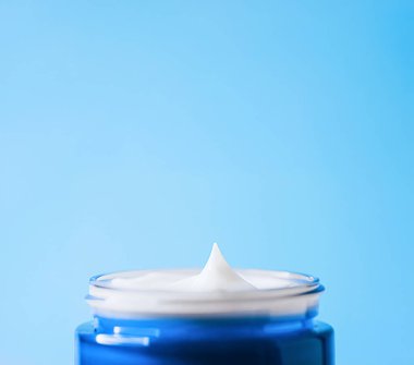 Krema ürünü, mavi bir kavanozun içinde parlak mavi bir arkaplanı temsil eden, cilt bakımını, güzelliği ve hidrasyonu temsil eden mükemmel bir zirve.