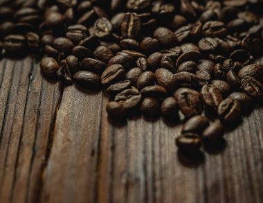 Kavrulmuş kahve çekirdekleri koyu ahşap bir zemin üzerinde zengin dokulu bir zemin oluşturarak sabah enerjisini ve aromasını sembolize ediyor.