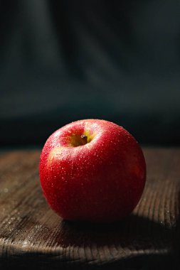 Taze kırmızı elma su damlalarıyla kaplı, koyu kırsal ahşap yüzeyde dinleniyor, sağlıklı beslenmeyi vurguluyor.