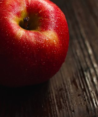 Su damlalarıyla kaplı canlı kırmızı elma, koyu ahşap bir yüzeyde dinleniyor, tazeliği ve sağlıklı besinleri vurguluyor.