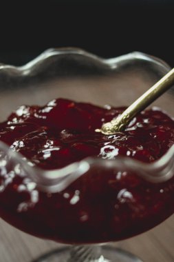 Kırmızı meyve reçeli bir tatlı kasesini dekoratif altın kaşıkla dolduruyor, lezzetli, doğal ve taze bir ikram sunuyor.