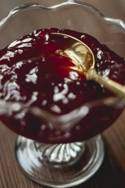 Küçük altın kaşıklı deniz tarağı dolu cam bir kasede kiraz reçeli tatlı bir yemek ya da tatlı olarak servis edilmeye hazır.