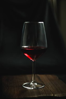 Bardağa dökülen kırmızı şarap zengin, karanlık bir estetik oluşturuyor, güzel bir akşam yemeğini, akşam içkilerini ve ahşap masada lüks bir tat alma deneyimini kutluyor.