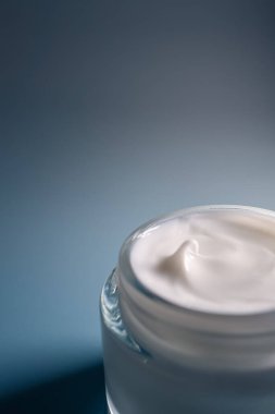 Yüz kremi kavanozu gelişmiş cilt bakımı sunuyor, mavi arka planda güzellik, sağlık ve sağlığı teşvik ediyor.