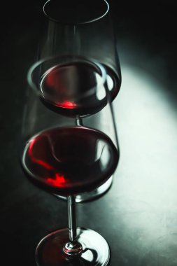 Koyu bir yansıtıcı yüzeyde iki zarif bardağa doldurulmuş kırmızı şarap, sofistike ve keyifli bir ortam yaratıyor.