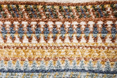 Yumuşak örülmüş kumaş arka planında, detaylı, sıcak bir geometrik desen ve doku gösteren yakın görünüm