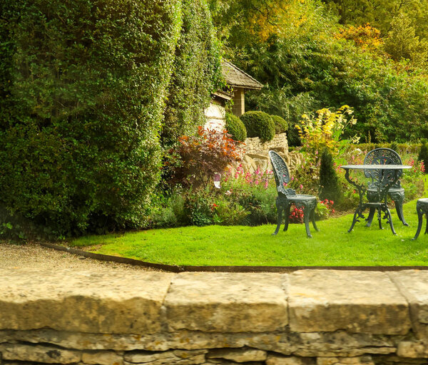 Outdoor garden featuring stone paved patio, green lawn, traditional furniture, and blooming flowers in a peaceful serene setting