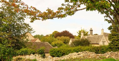 Geleneksel taştan kulübeleri, kuru bir taş duvarı ve mevsimsel sonbahar renklerini gösteren ağaçlarıyla Cotswold köyünü büyülüyor.