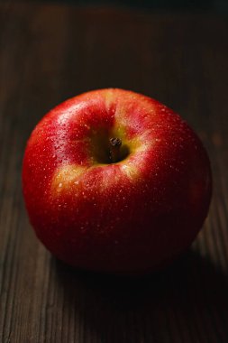 Koyu bir ahşap yüzeyde dinlenen parlak su damlacıklarıyla kaplı sulu kırmızı elma tazeliği ve sağlıklı yaşam tarzını vurguluyor.