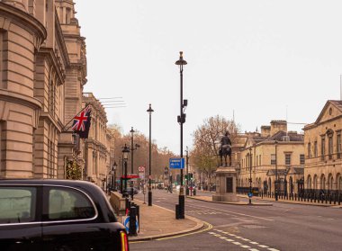İngiliz bayrağı, klasik mimari ve arka planda tarihi bir binicilik heykeli ile Whitehall, Londra 'dan geçen siyah bir taksi.