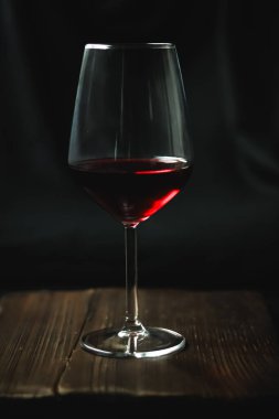 Bardakta kırmızı şarap, koyu ahşap bir yüzey üzerinde zengin bir yakut parıltısı yaratır. Bir rahatlama anı ve sofistike bir ortam yakalıyorum.