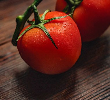 Sarmaşıkta ıslak, olgun domatesler taze ve sağlıklı besleniyor. Koyu ahşap bir yüzeyde su damlacıkları var.