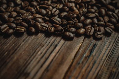 Kavrulmuş kahve çekirdekleri, canlandırıcı içeceklerin temel unsurunu temsil eden koyu, sade ahşap bir masaya yayılmış.