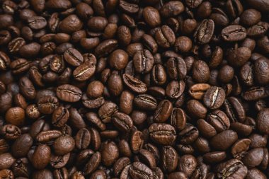 Kavrulmuş kahve çekirdekleri aromayı, enerjiyi ve kahveye olan sevgiyi temsil eden zengin, dokulu bir arka plan oluşturuyor.