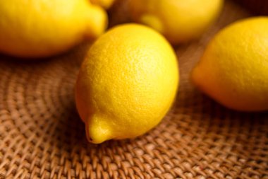 Kahverengi bir hasır arka plana yerleştirilmiş parlak sarı limonlar doğal ve taze narenciye meyveleri sergiliyor.